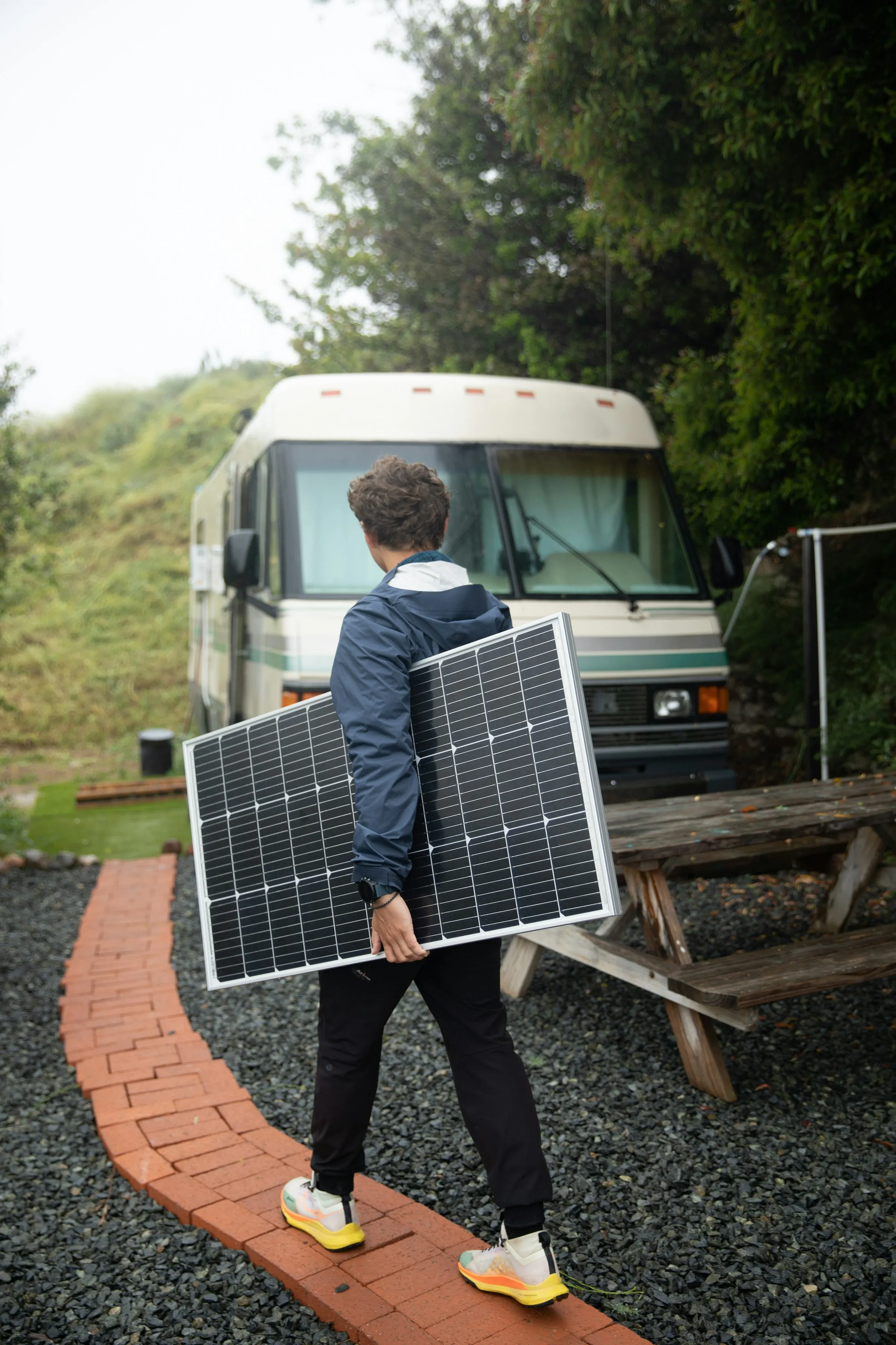 A technician carrying a solar panel toward an RV parked in a campground